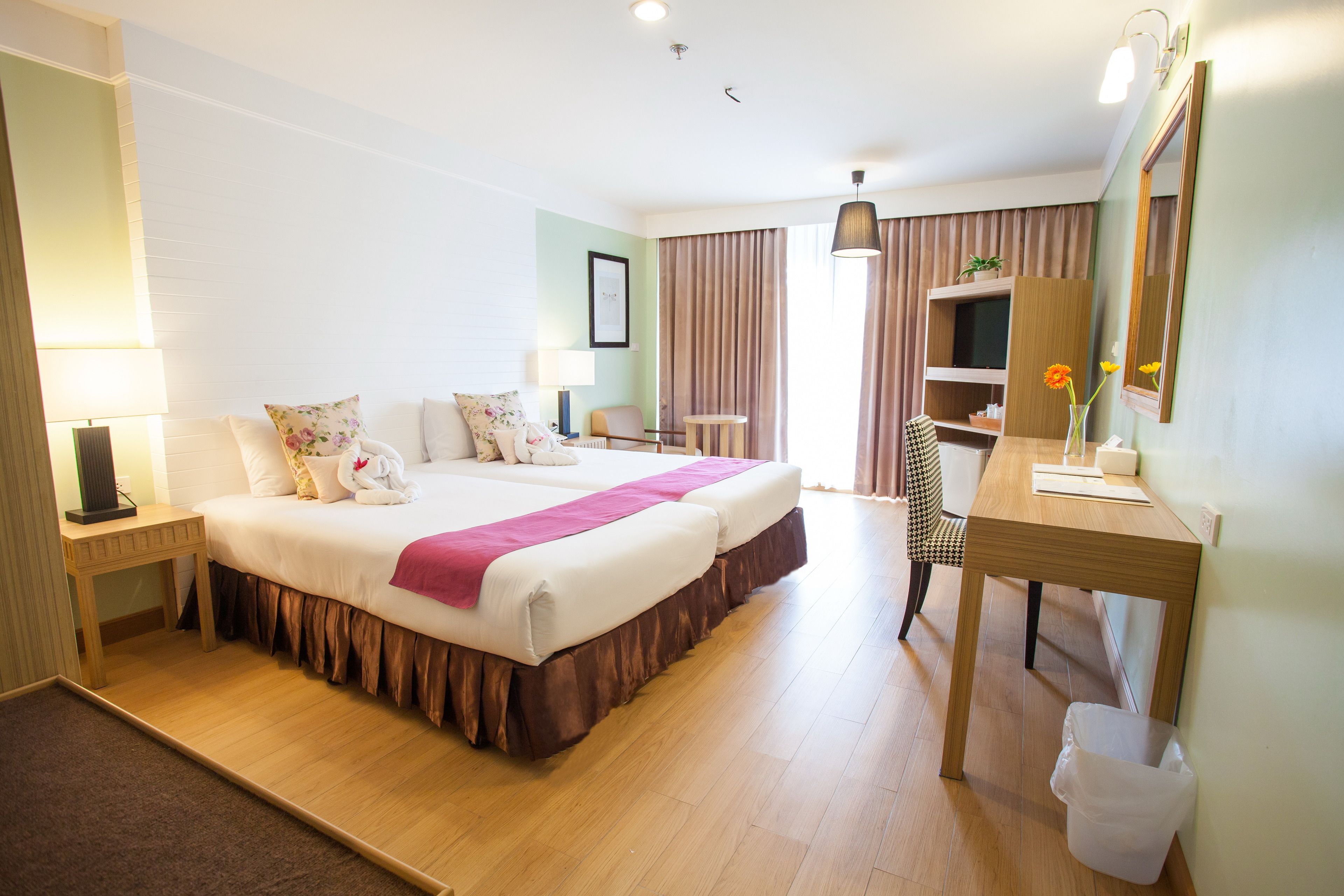 Habitación de hotel con cama doble, escritorio con silla, mesita, lámpara, espejo y cesto de basura.
