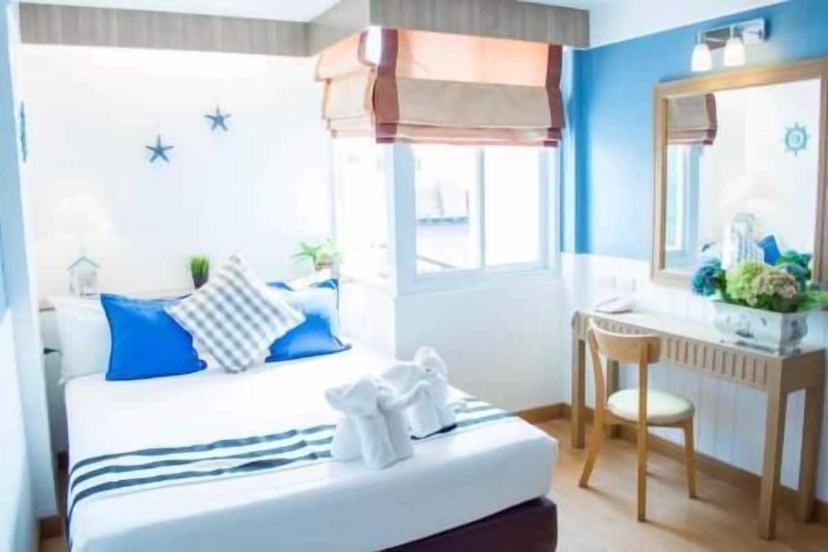 A hotel room with a bed, a desk, a chair, a window, and a mirror.