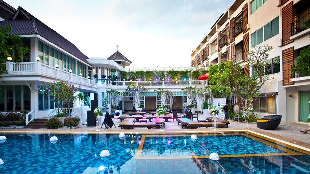 A swimming pool with a tiled deck, surrounded by lounge areas and outdoor seating. - Paradise Hotel (Udon Thani)