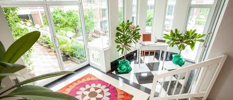 A spacious balcony with large windows, a modern staircase, and a variety of potted plants.