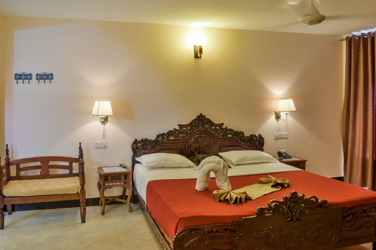 Une chambre d’hôtel avec un lit à baldaquin en bois, deux tables de chevet, une petite table, une chaise et une couverture de lit rouge.