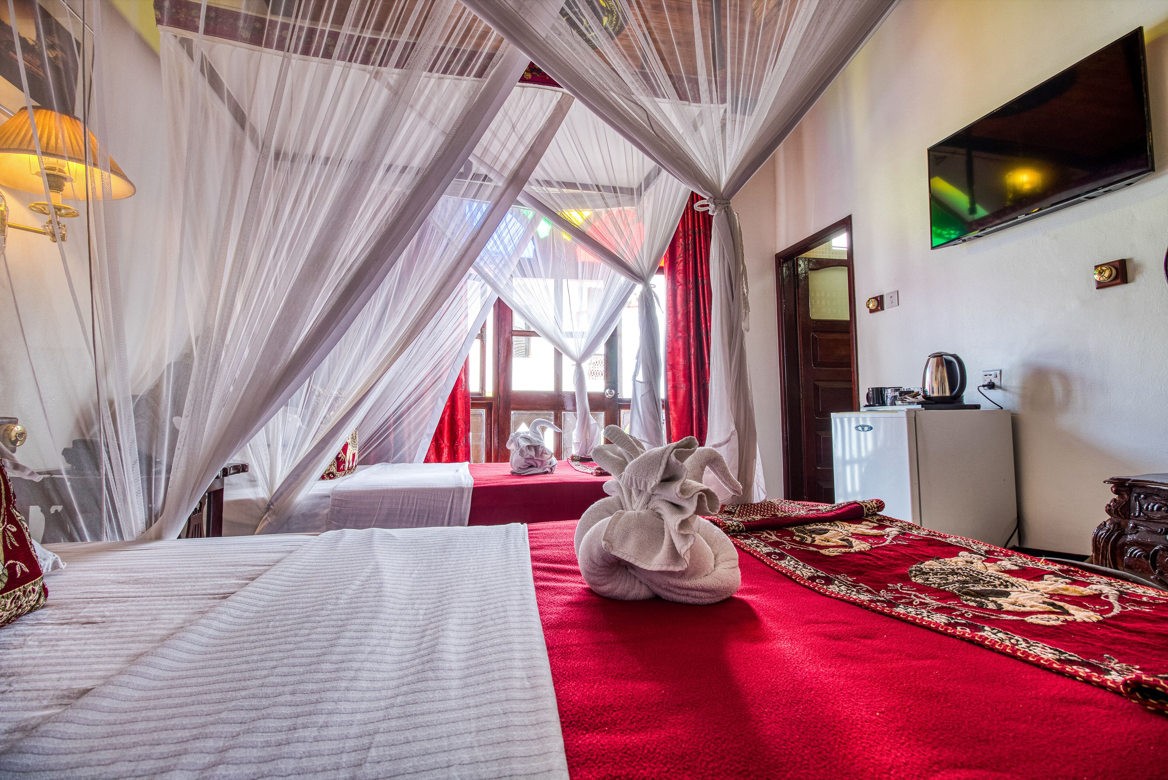 A hotel room with a bed, a red carpet, a TV, and a minibar.