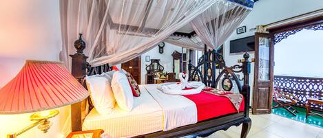 A four-poster bed with a canopy, a red bedspread, and a wooden nightstand with a lamp.