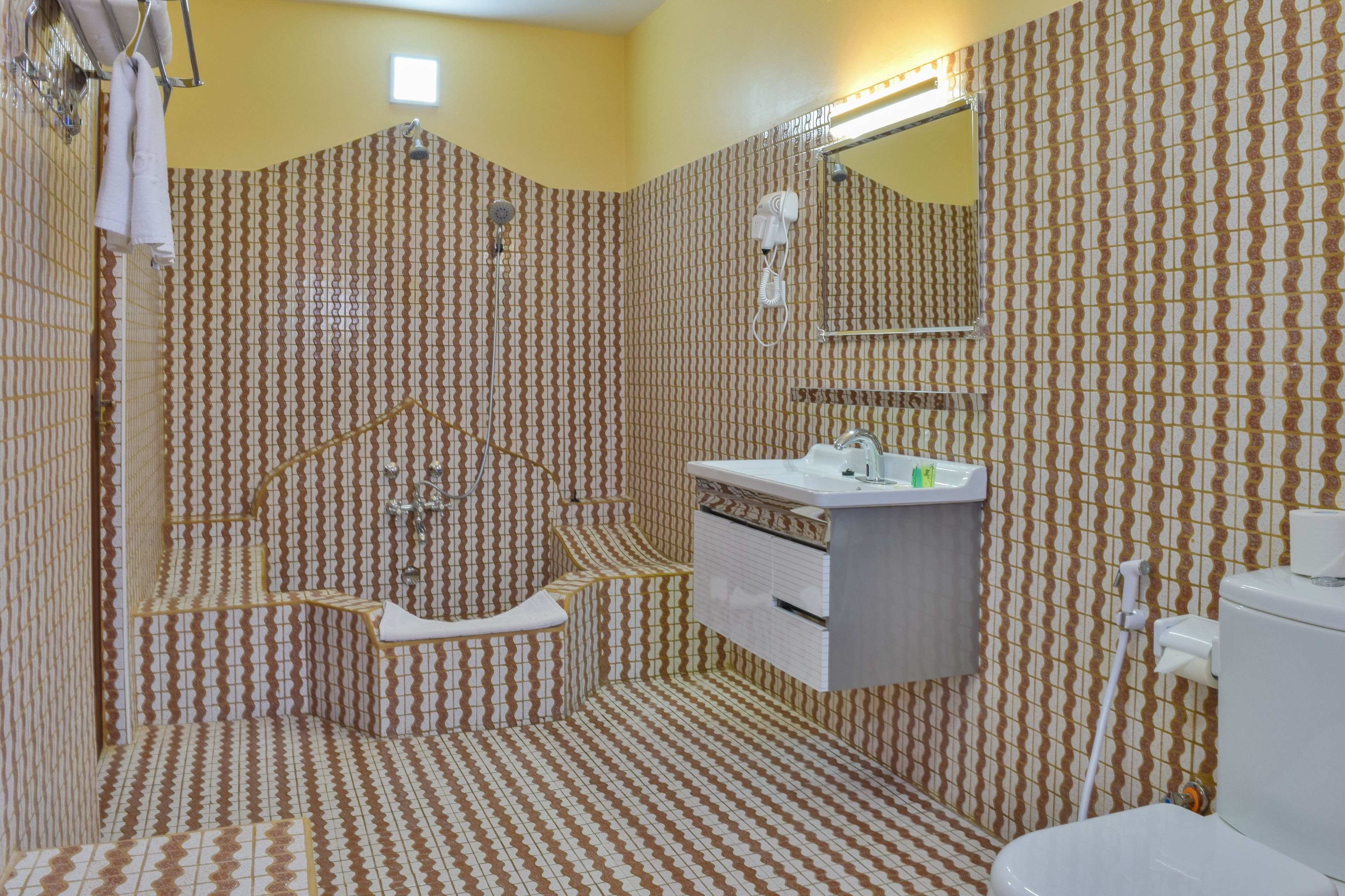 A bathroom with patterned wallpaper, a shower, a sink, and a toilet.