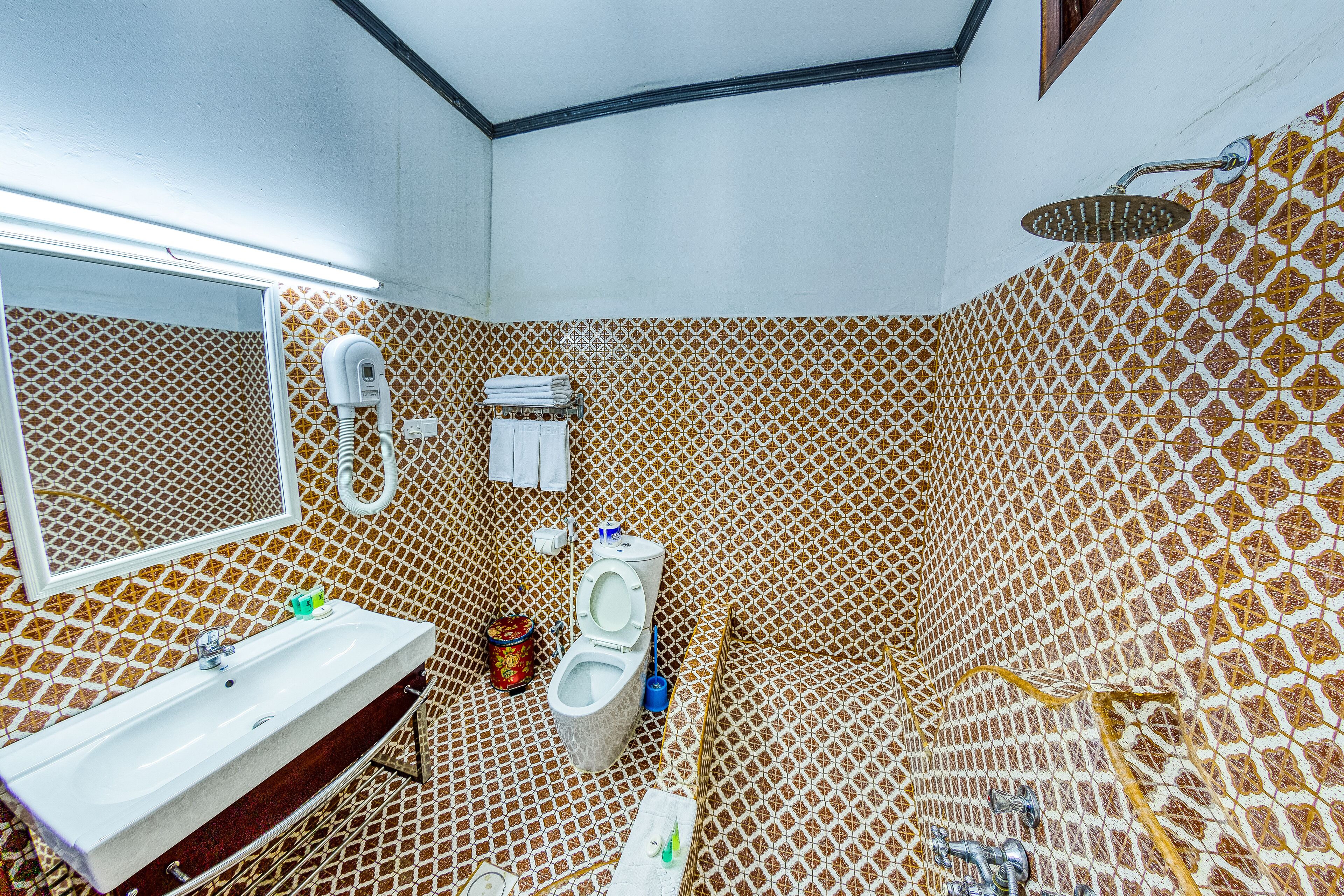 Un baño con pared de azulejos estampados, un lavabo, un inodoro y una zona de ducha.
