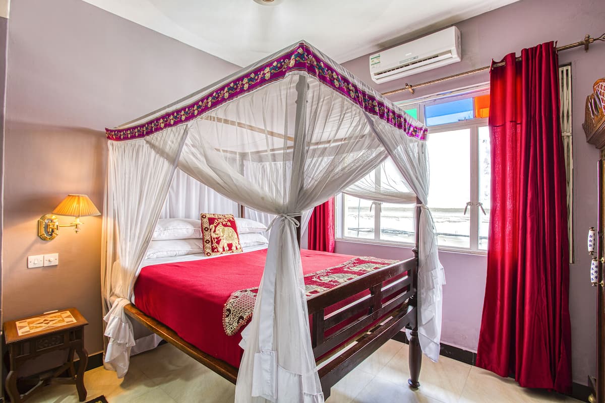 Un lit à baldaquin avec une couvre-lit rouge, des rideaux blancs et une moustiquaire.