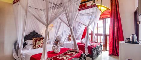 A four-poster bed with white canopy, red bedspread, and decorative pillows.