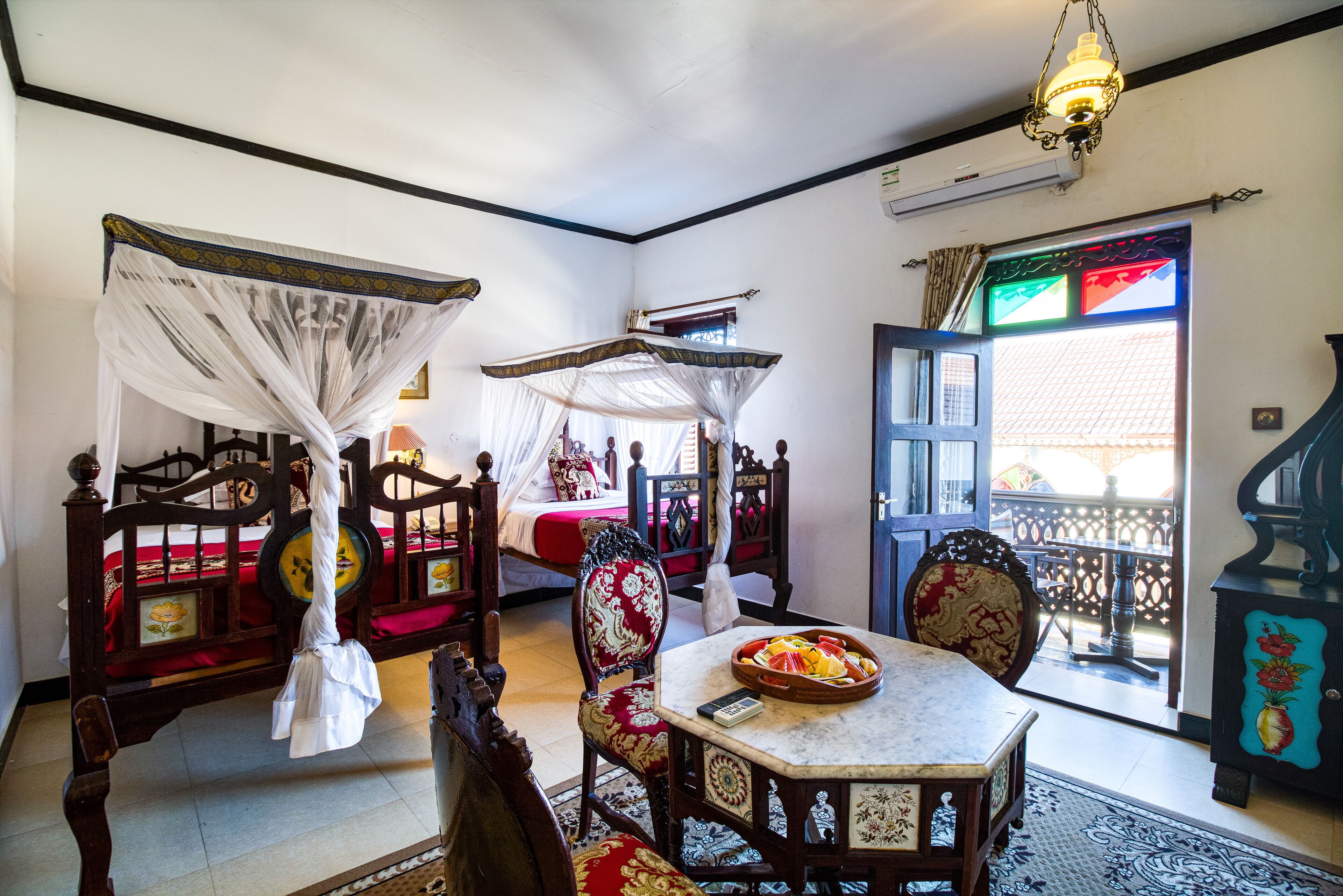 A traditional room with a bed, a table with fruit, a chair, and a balcony with a railing.