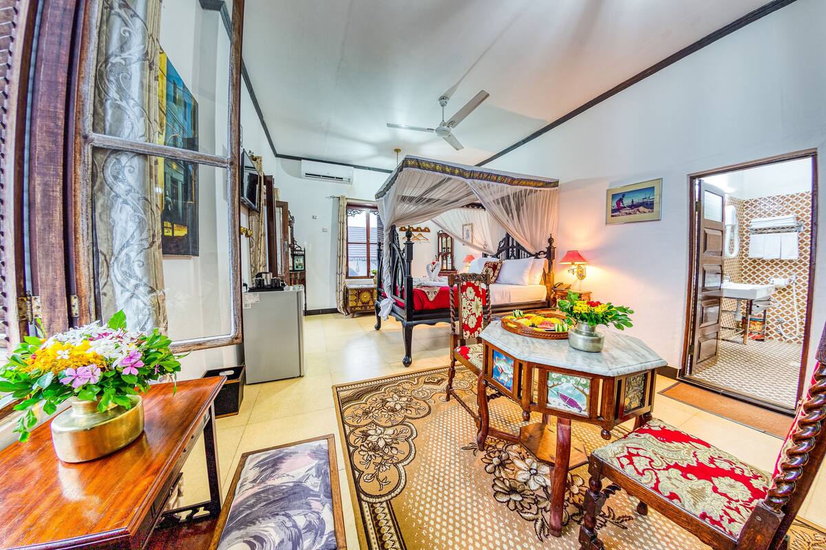 Une chambre avec un lit, une table de chevet avec une lampe, un miroir et une fenêtre avec des rideaux.