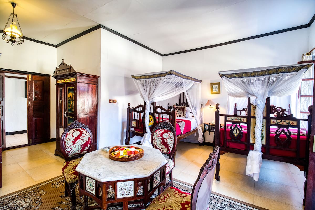 Une chambre traditionnelle avec un lit, une armoire en bois, une table sur laquelle se trouve un panier de fruits et un fauteuil suspendu.