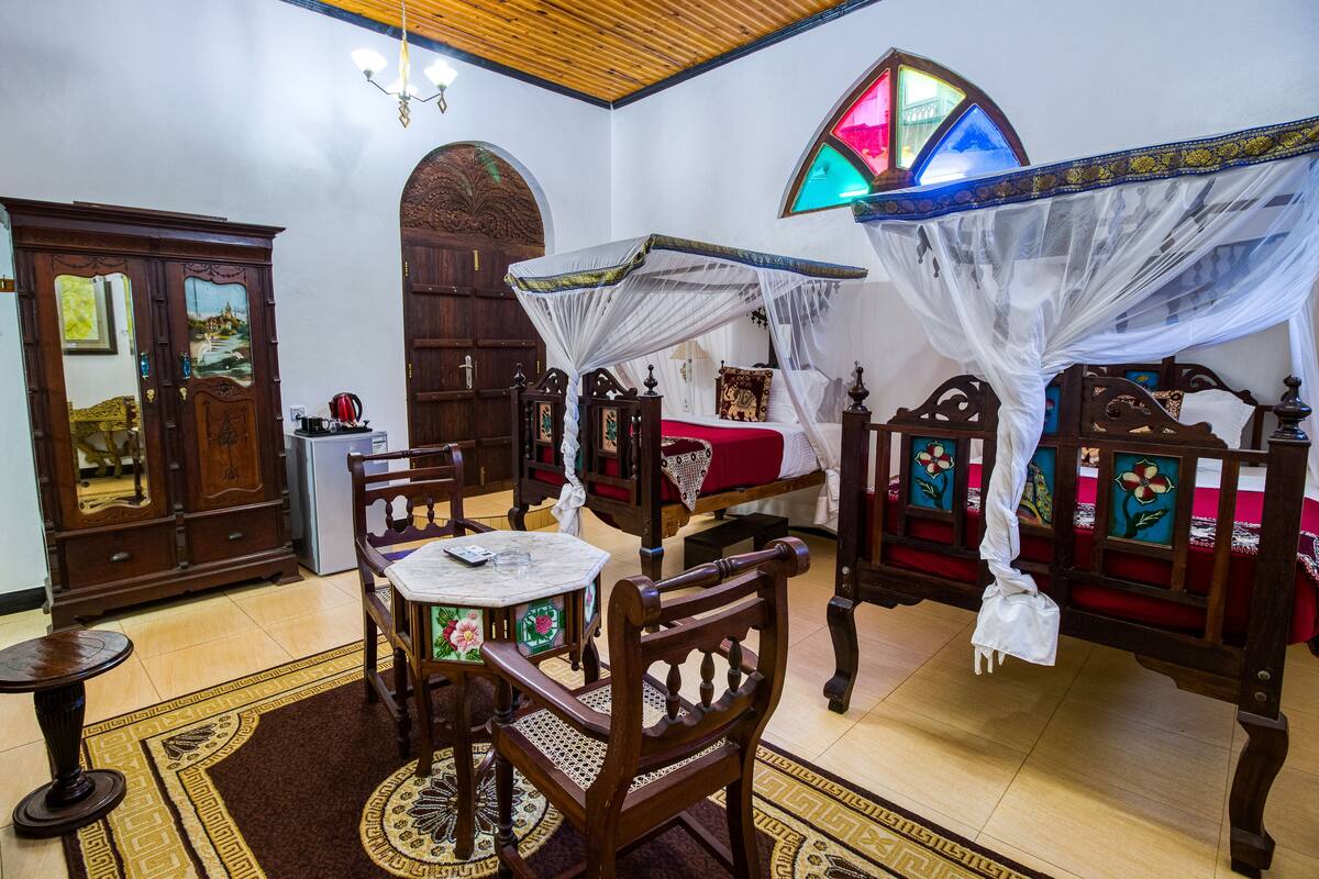 Une chambre à l’ancienne, avec un lit à baldaquin, une armoire en bois, une petite table et un tapis décoratif.