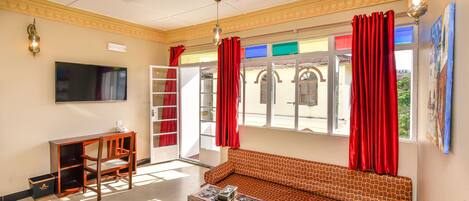 A living room with a sofa, a coffee table, a TV, and a window with red curtains.