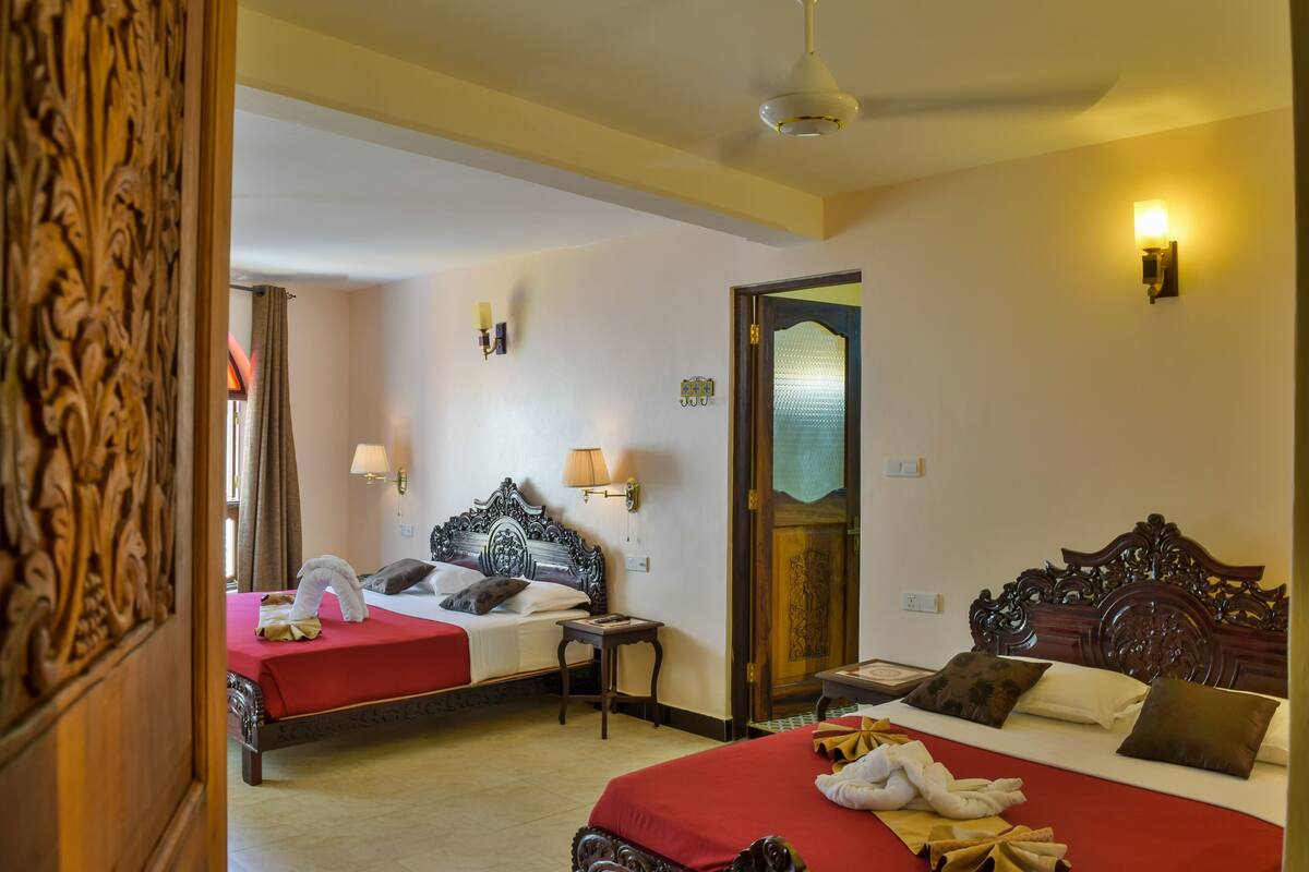 Une chambre d’hôtel avec deux lits, chacun recouvert d’une couverture rouge, dotée d’une tête de lit en bois et de lampes de chevet.
