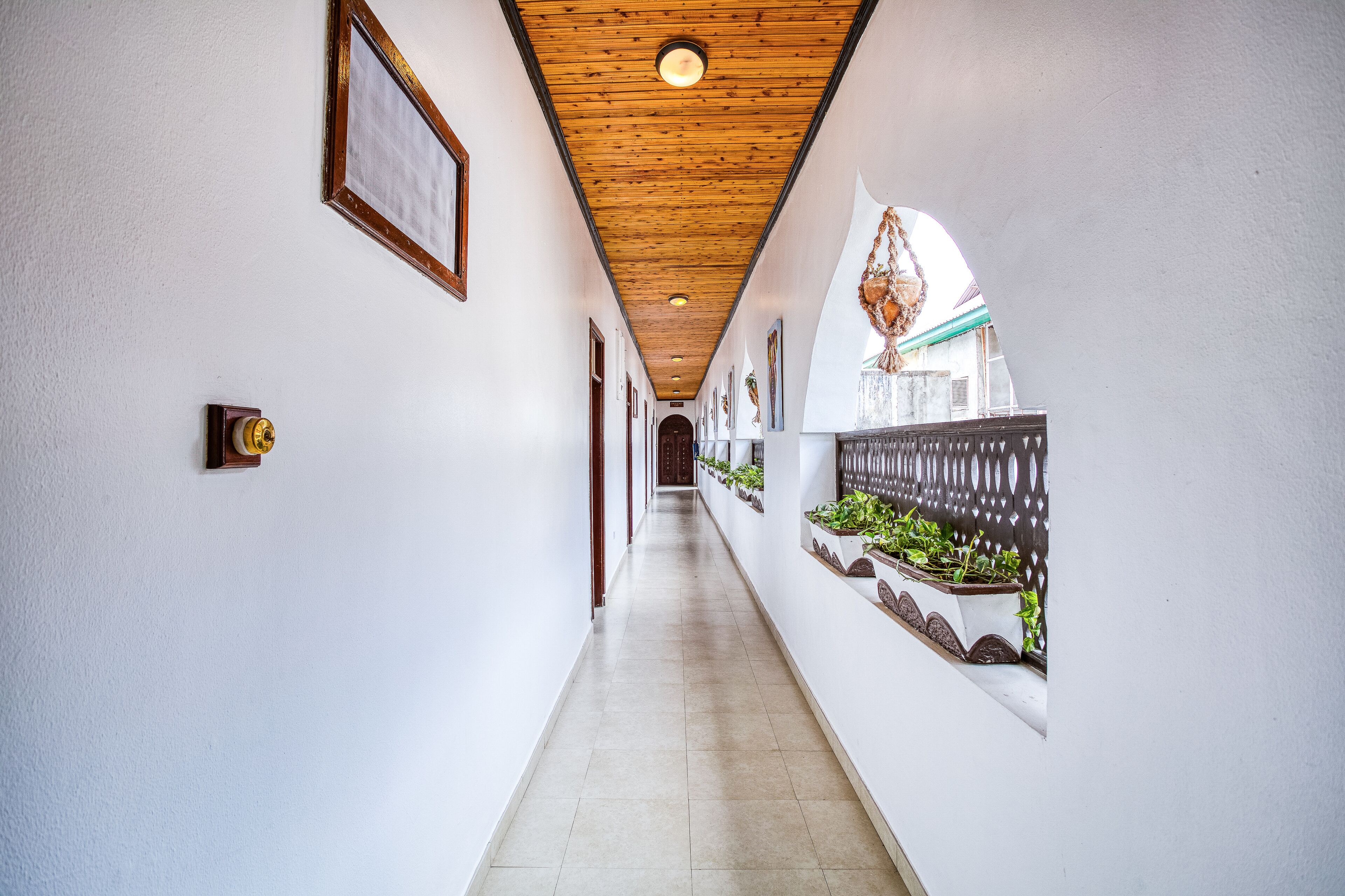A corridor with wooden ceiling, framed pictures, and potted plants along the walls.
