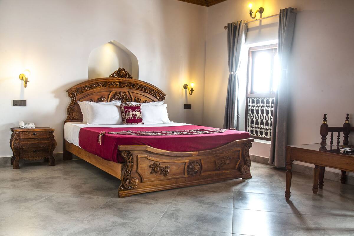 Une chambre à coucher avec un lit en bois, deux tables de chevet, une commode, une fenêtre avec des rideaux et une petite table.