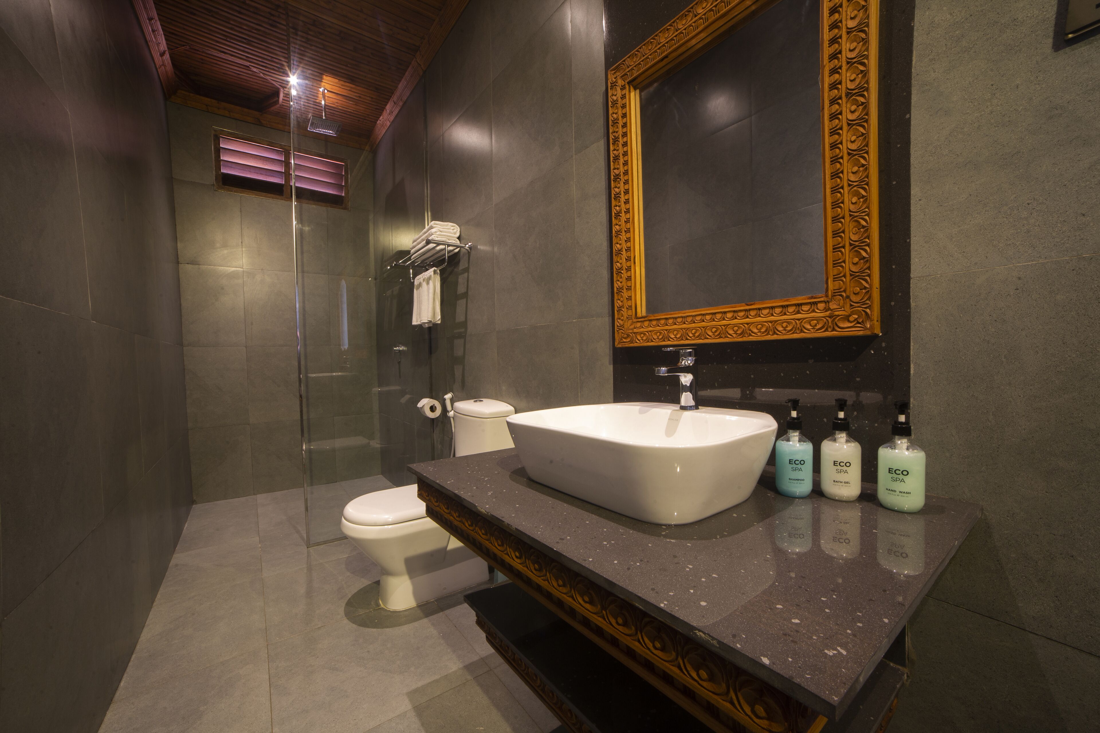 A modern bathroom with a large mirror, a sink, and three bottles of shampoo.