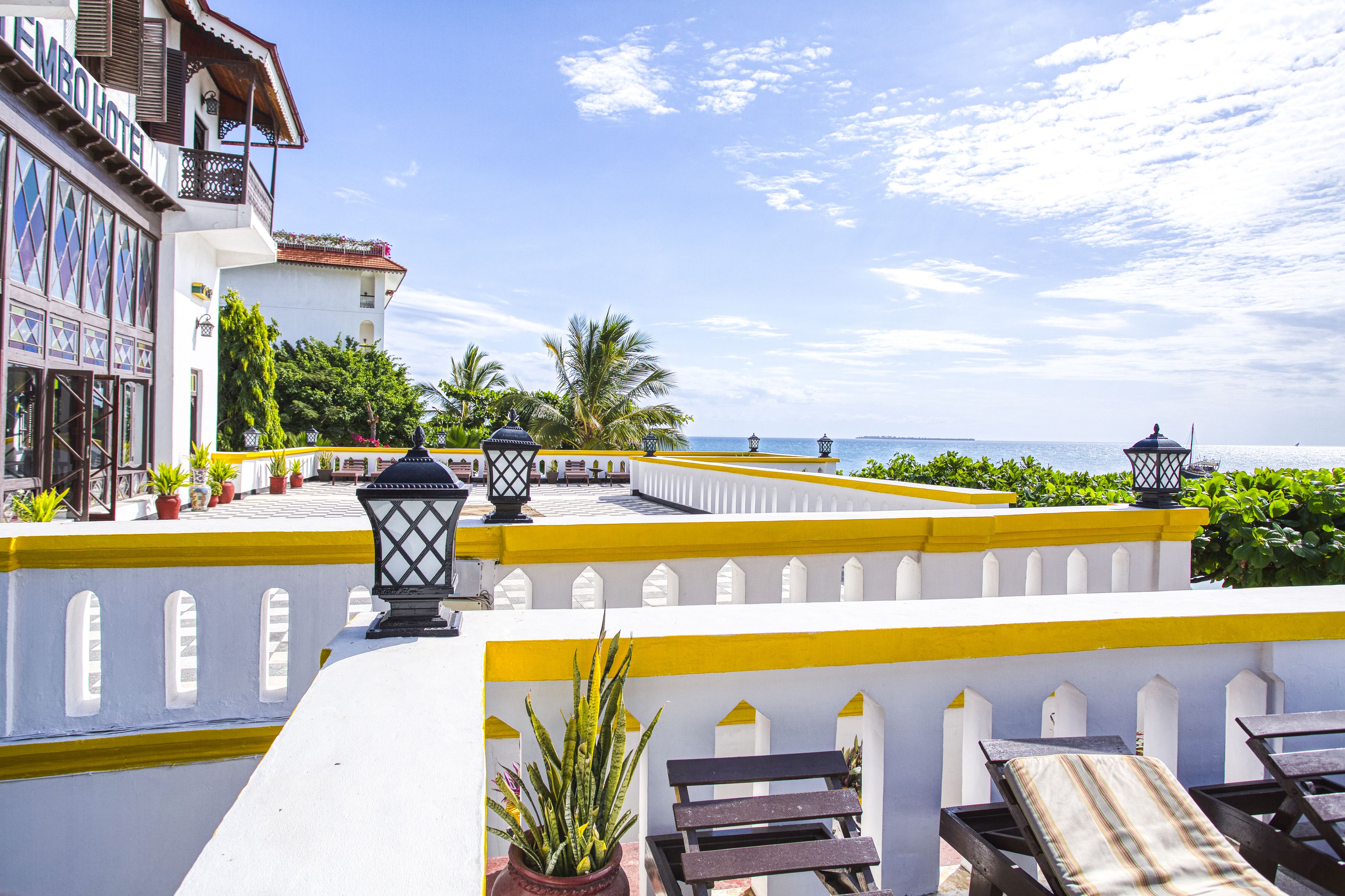 A hotel with a balcony overlooking the sea, featuring potted plants and outdoor seating.