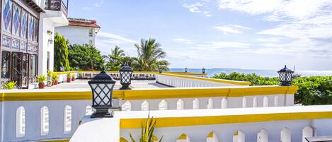 A hotel with a balcony overlooking the sea, featuring potted plants and outdoor seating.