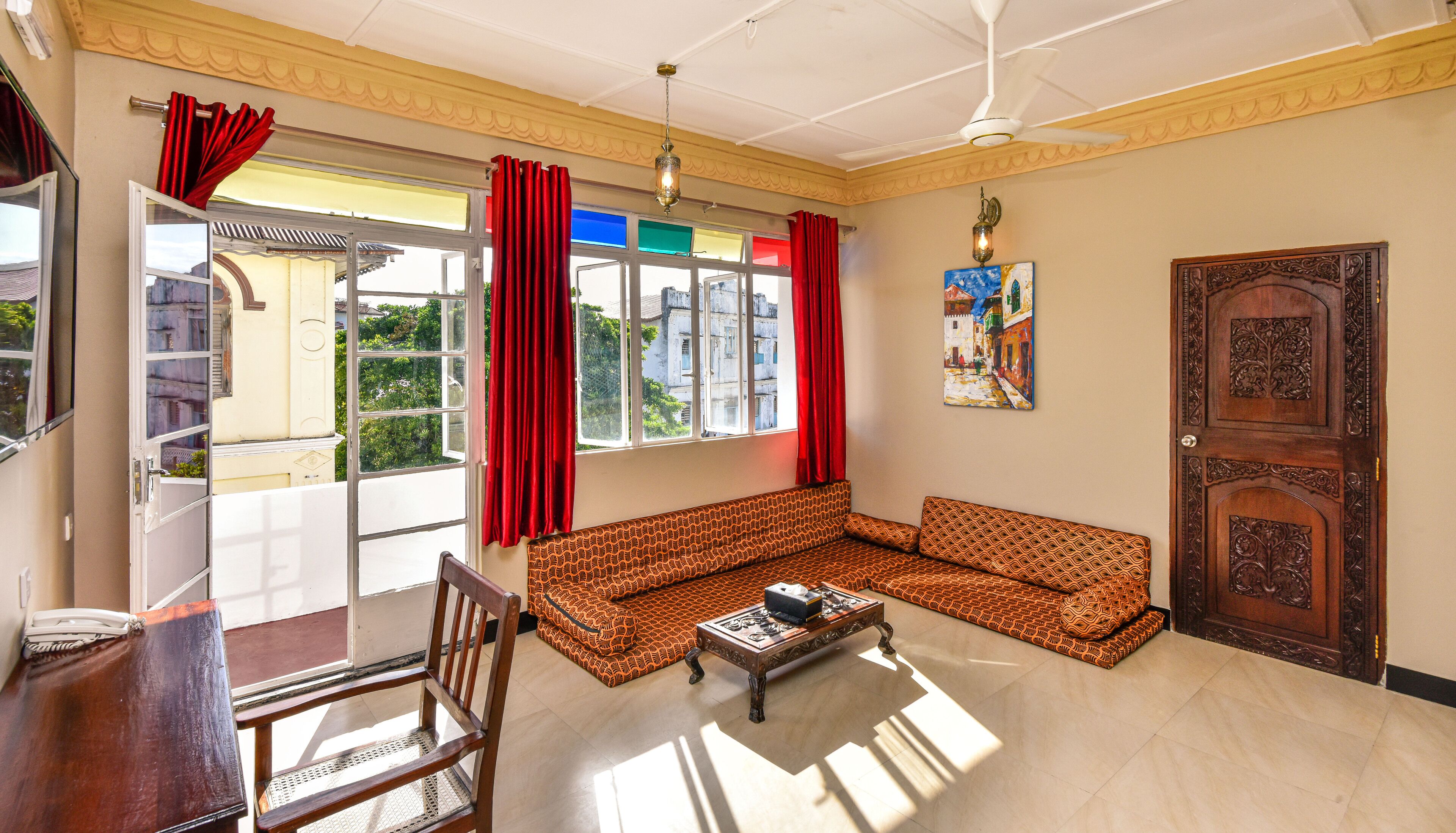 A living room with a sofa, a coffee table, a chair, a wooden door, and a window with red curtains.