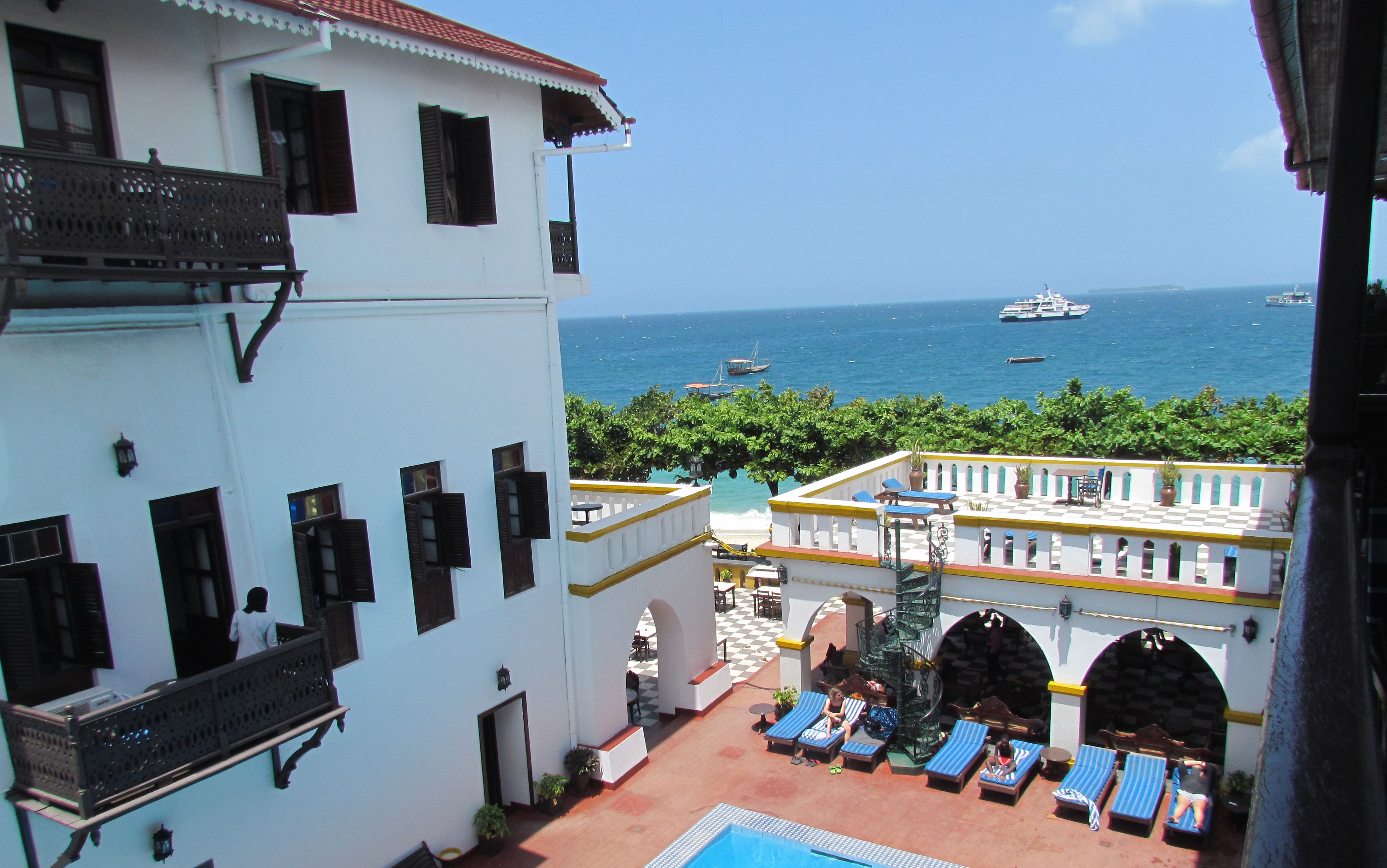 Un hôtel doté d’une piscine, de chaises longues et offrant une vue sur la mer et les bateaux.