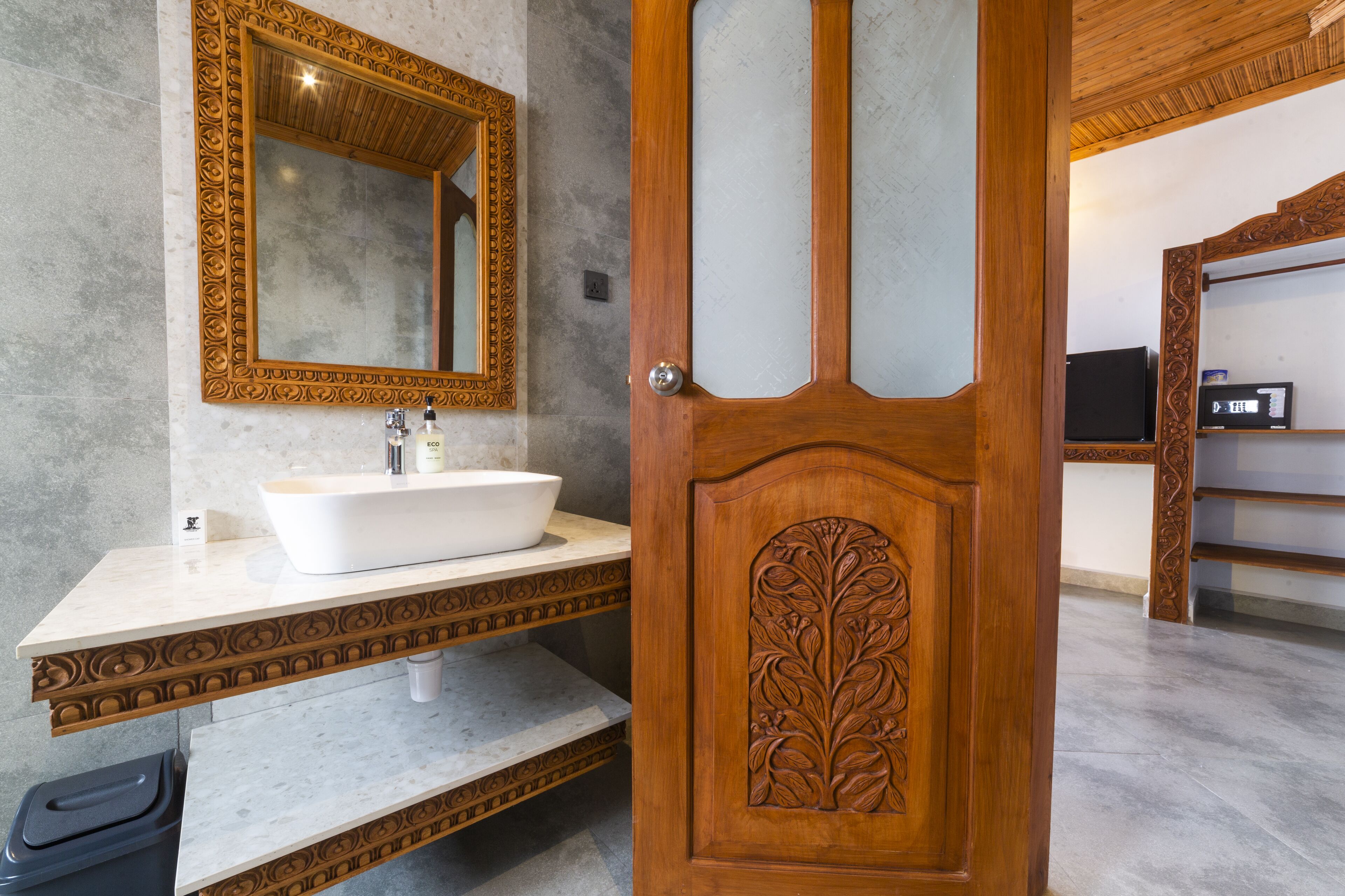A bathroom with a wooden door, a white sink, and a large mirror with an ornate frame.