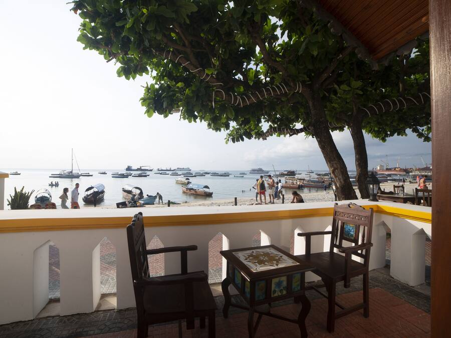 A terrace with wooden chairs and a table, overlooking a marina with boats and people.