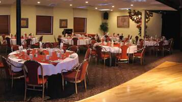 A banquet hall with round tables, chairs, and a stage area.