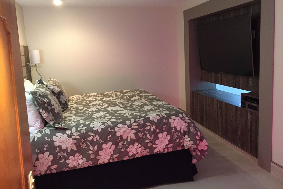 A bedroom with a bed, a TV mounted on the wall, and a wooden paneling design.