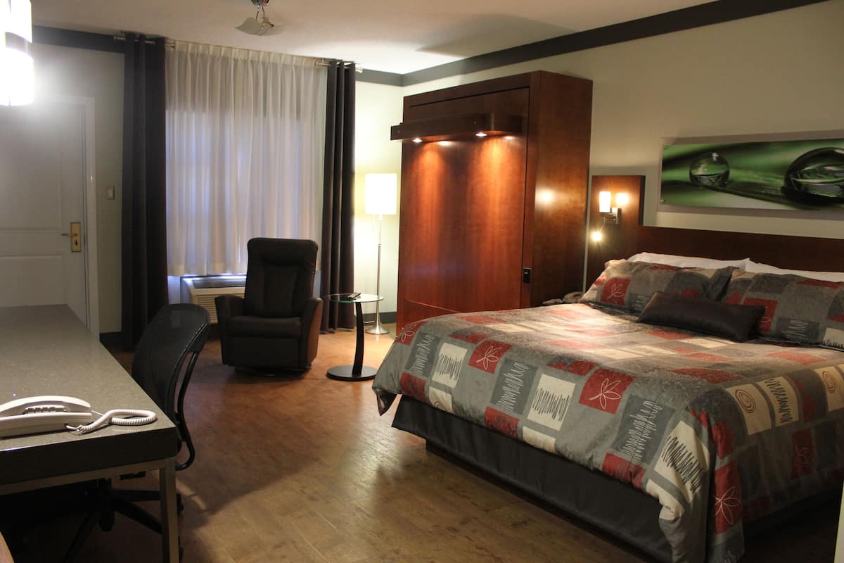 A hotel room with a bed, a desk with a telephone, a chair, a lamp, and a painting on the wall.