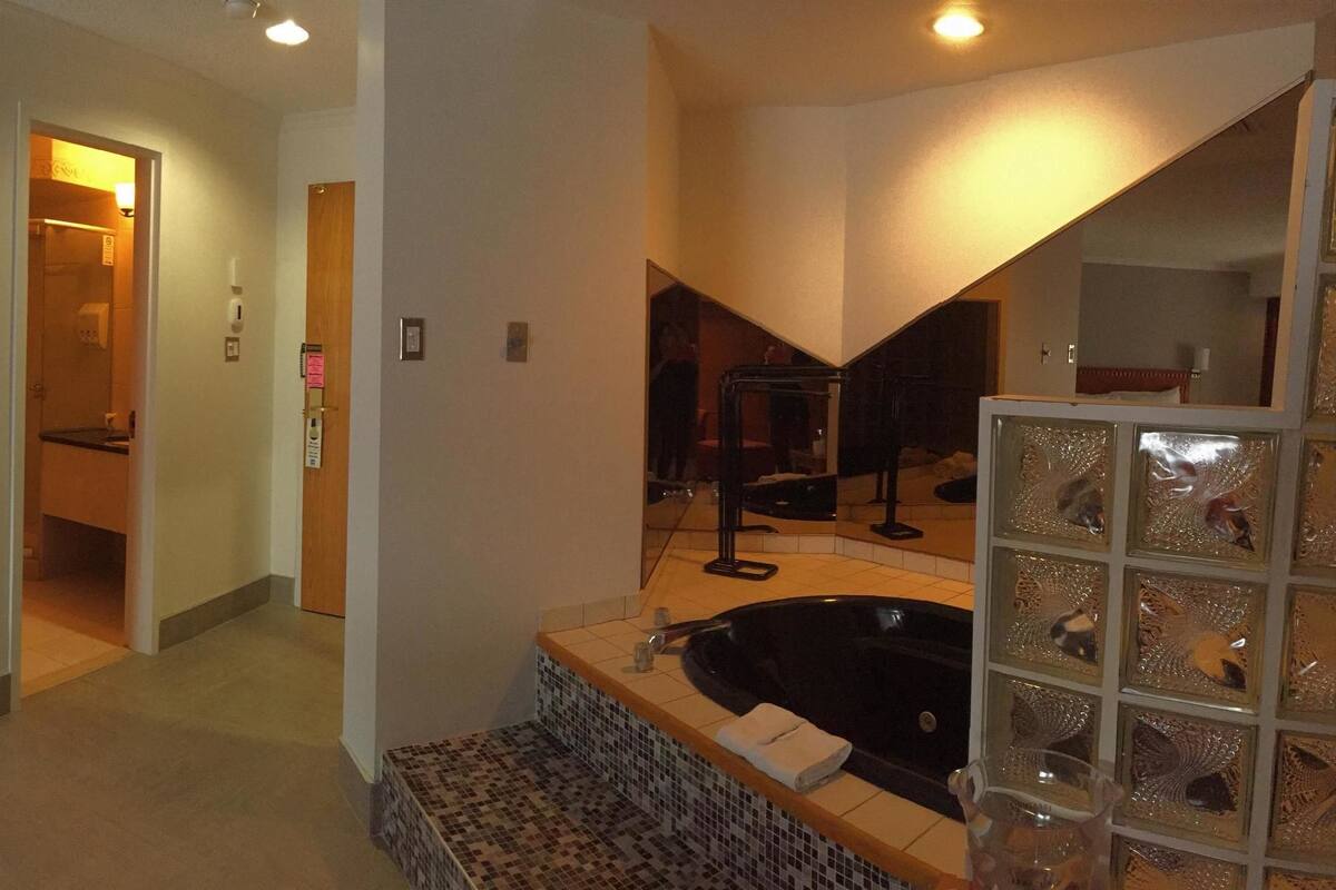 A hotel room with a bed, a chair, a bathroom with a bathtub, and a mirror.