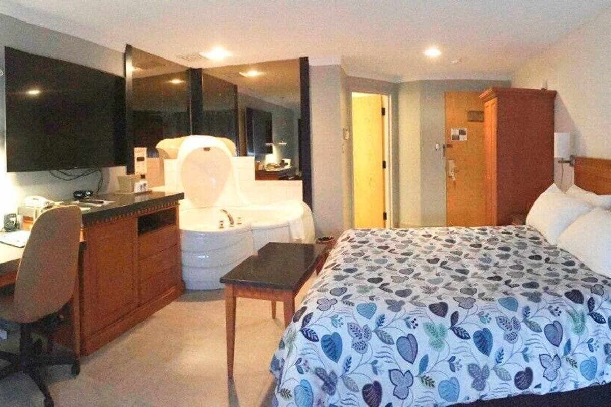 A hotel room with a bed, a desk with a computer, a chair, a television, and a bathroom.