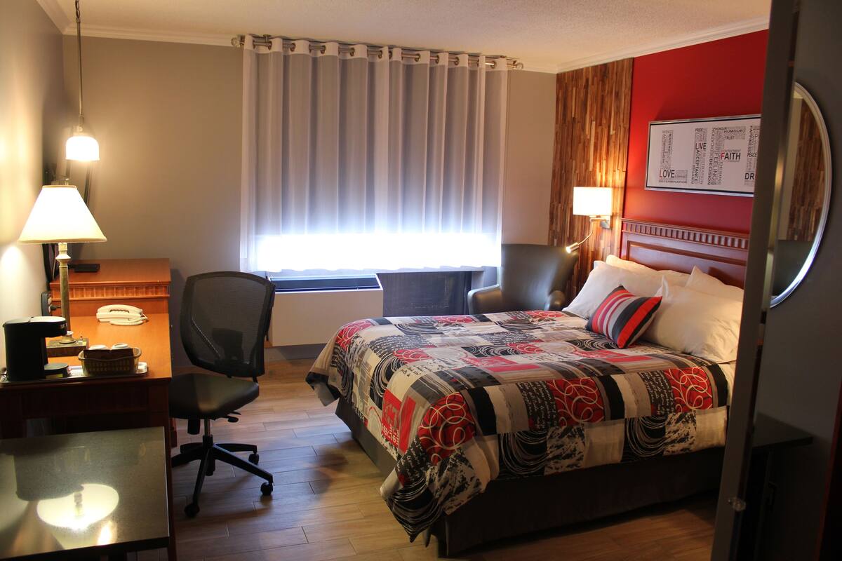 A hotel room with a bed, desk, chair, and a window with curtains.