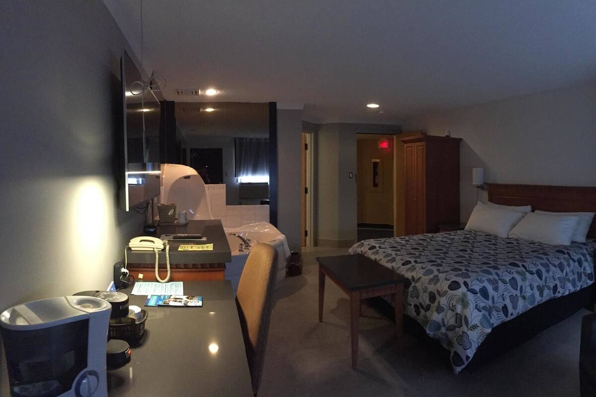 A hotel room with a bed, a desk with a telephone, a chair, and a mirror.