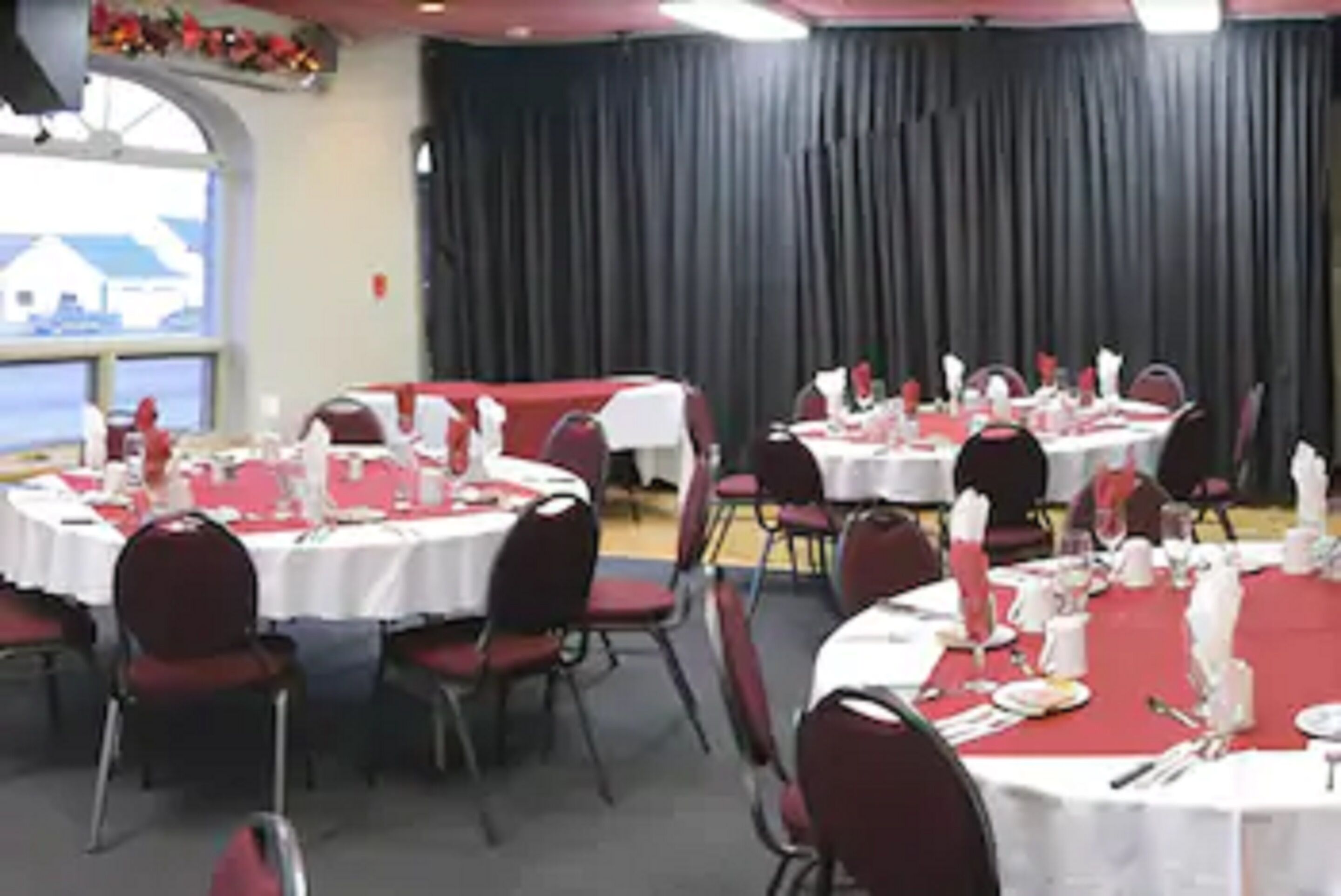 Un salón de banquetes con mesas redondas dispuestas para comer, sillas rojas y manteles blancos.