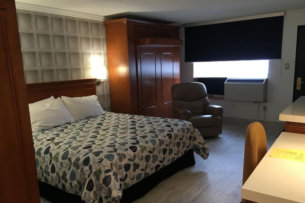 A hotel room with a bed, a wardrobe, a chair, a desk, and a window with blinds.