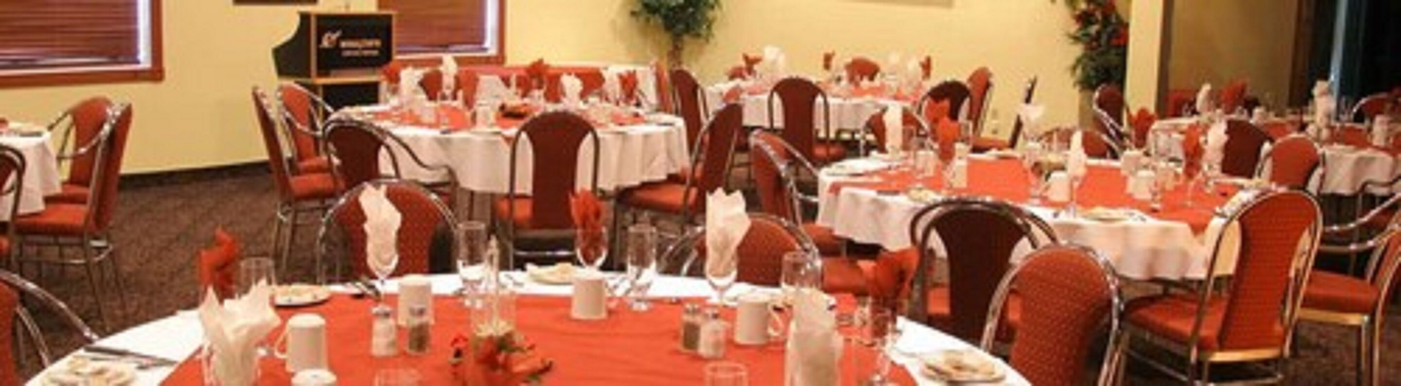 Una sala de banquetes amb taules rodones preparades per a dinar, cadascuna amb mantells blancs i cadires vermelles.