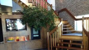 A modern interior with a wooden staircase, a large indoor plant, and a flat-screen TV mounted on the wall. - Amosphère Complexe hôtelier (Amos)