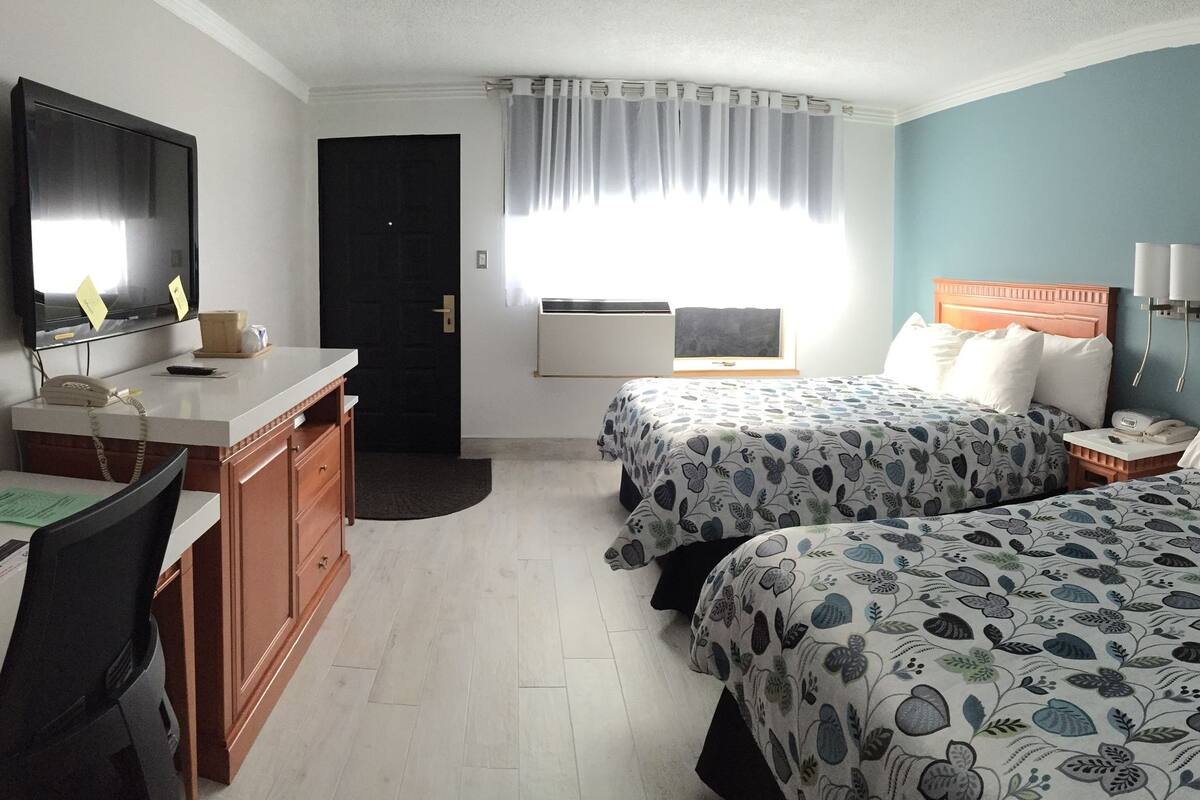 A hotel room with two beds, a desk with a telephone, a TV, and a chair.