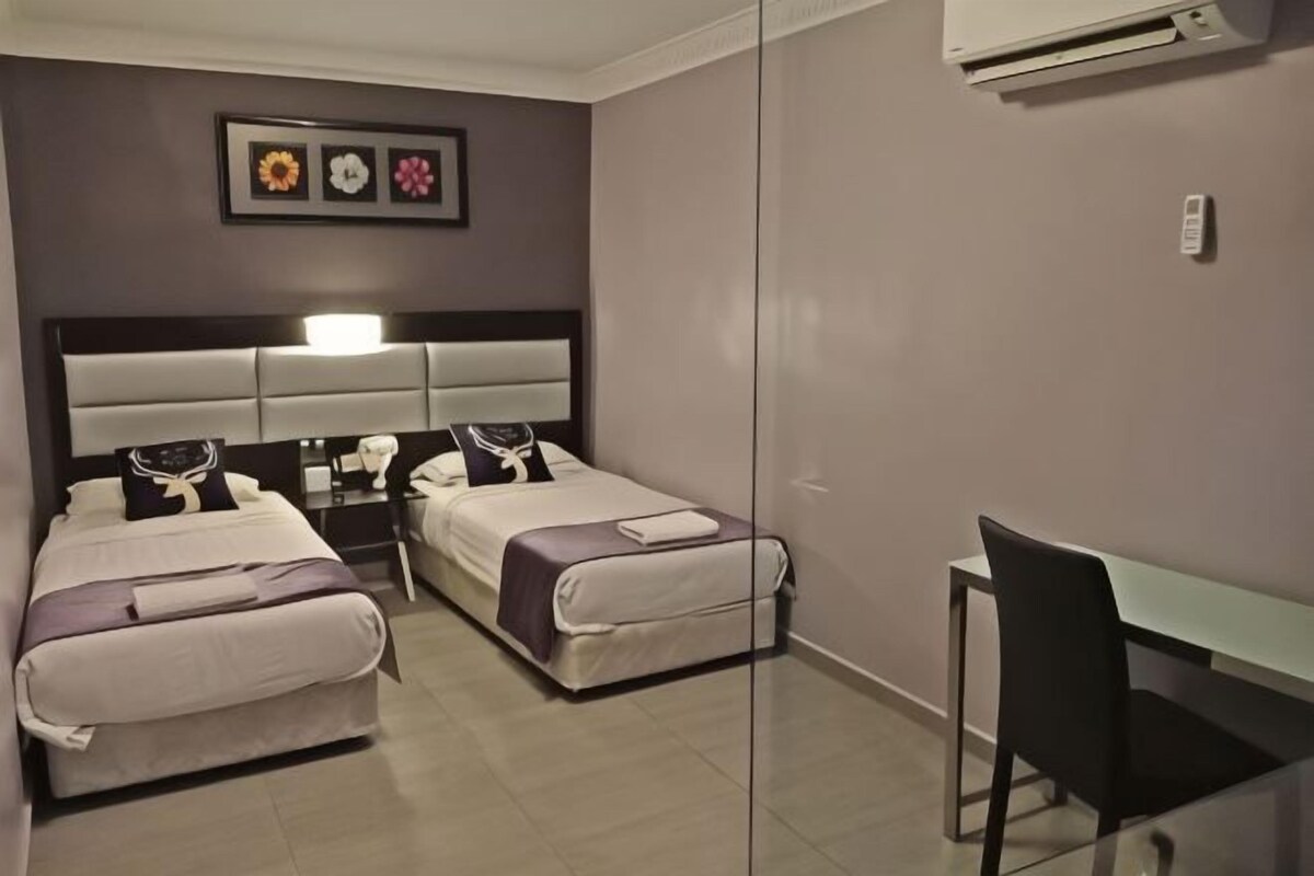 A hotel room with two beds, a desk, and an air conditioning unit.