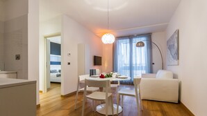 A modern living room with a white sofa, a dining table with chairs, and a chandelier. - MyApART Suite (Rome)