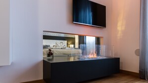 A modern living room with a flat-screen TV mounted on the wall, a glass-top coffee table with a fire feature, and a cozy seating area with a sofa and cushions. - MyApART Suite (Rome)
