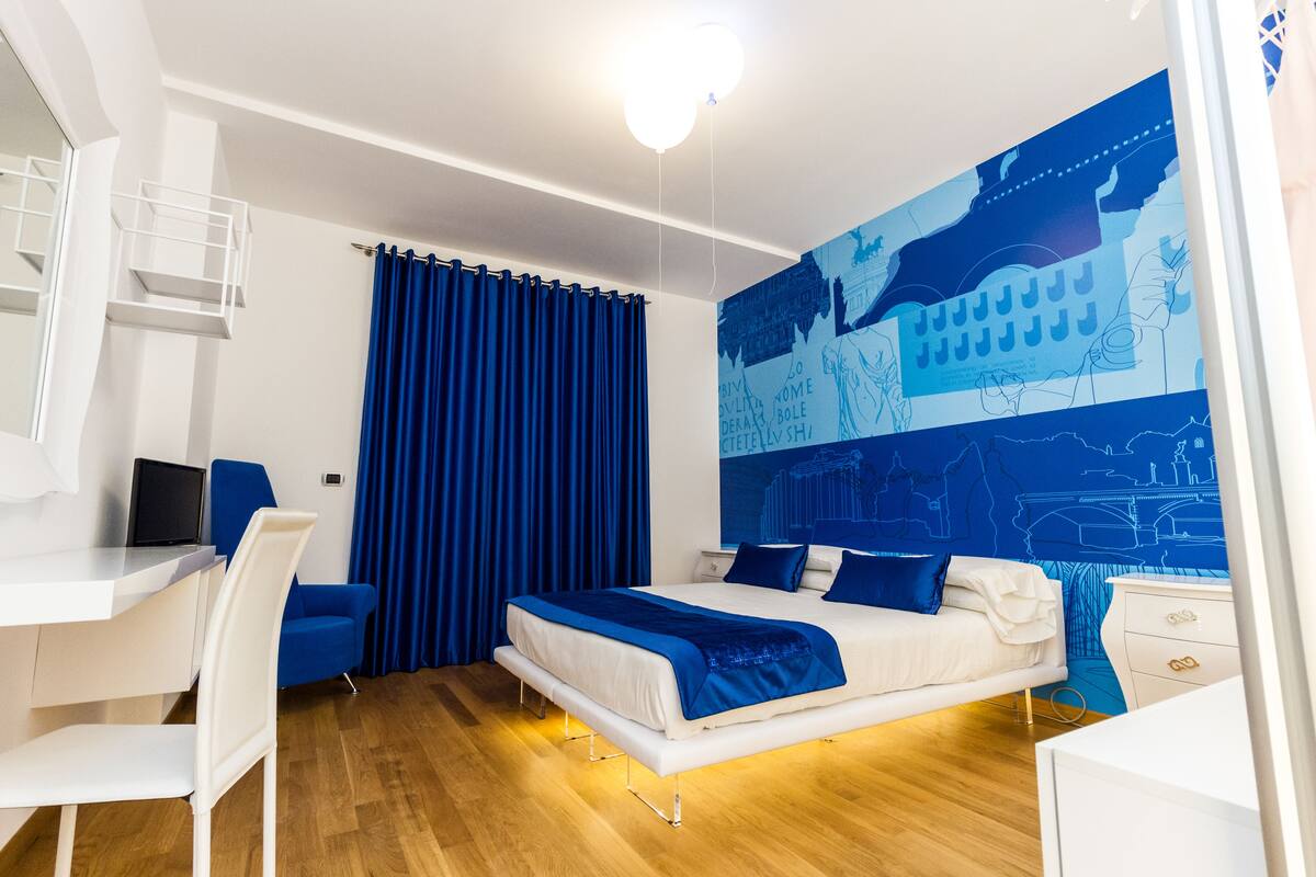 A modern bedroom with a bed, desk, chair, and a large blue mural on the wall.