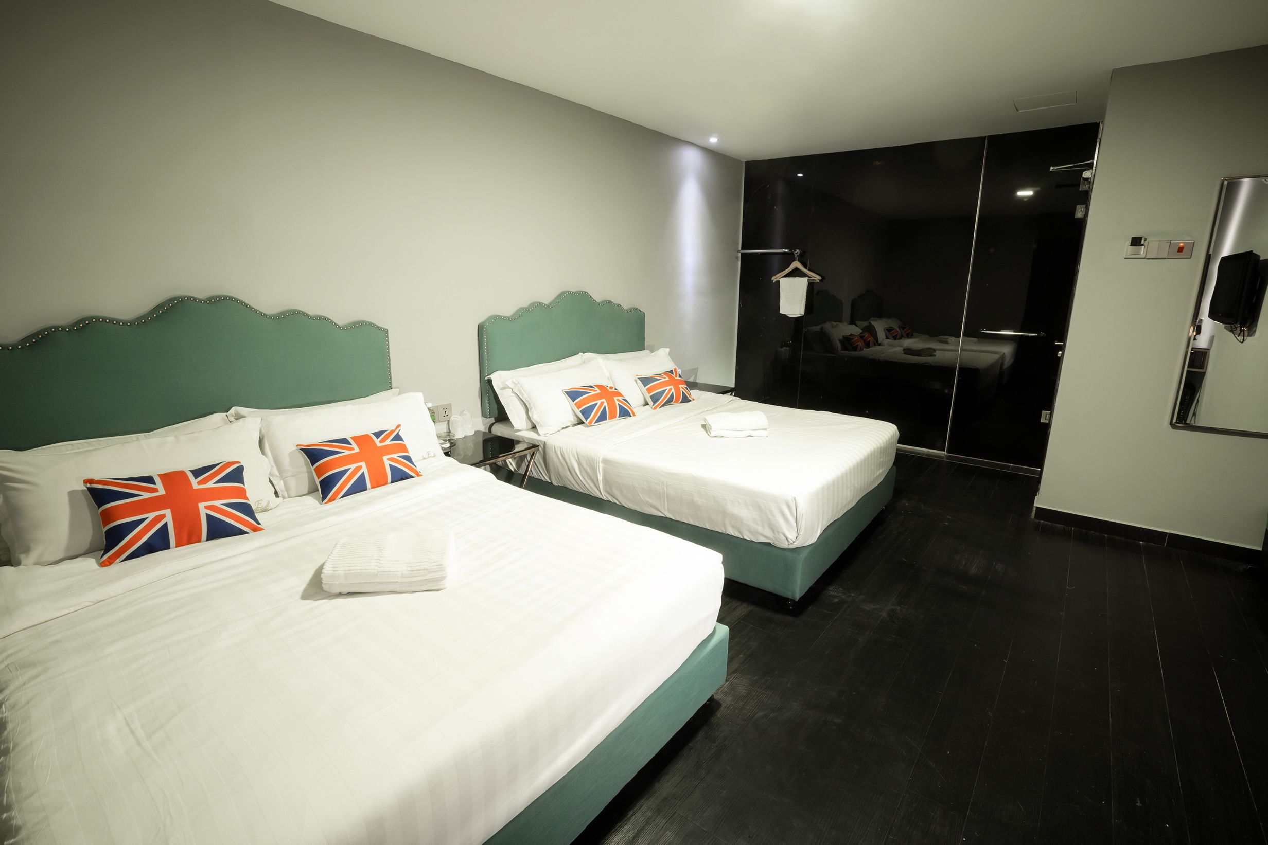 A hotel room with two beds, each with white bedding and pillows featuring the Union Jack flag.