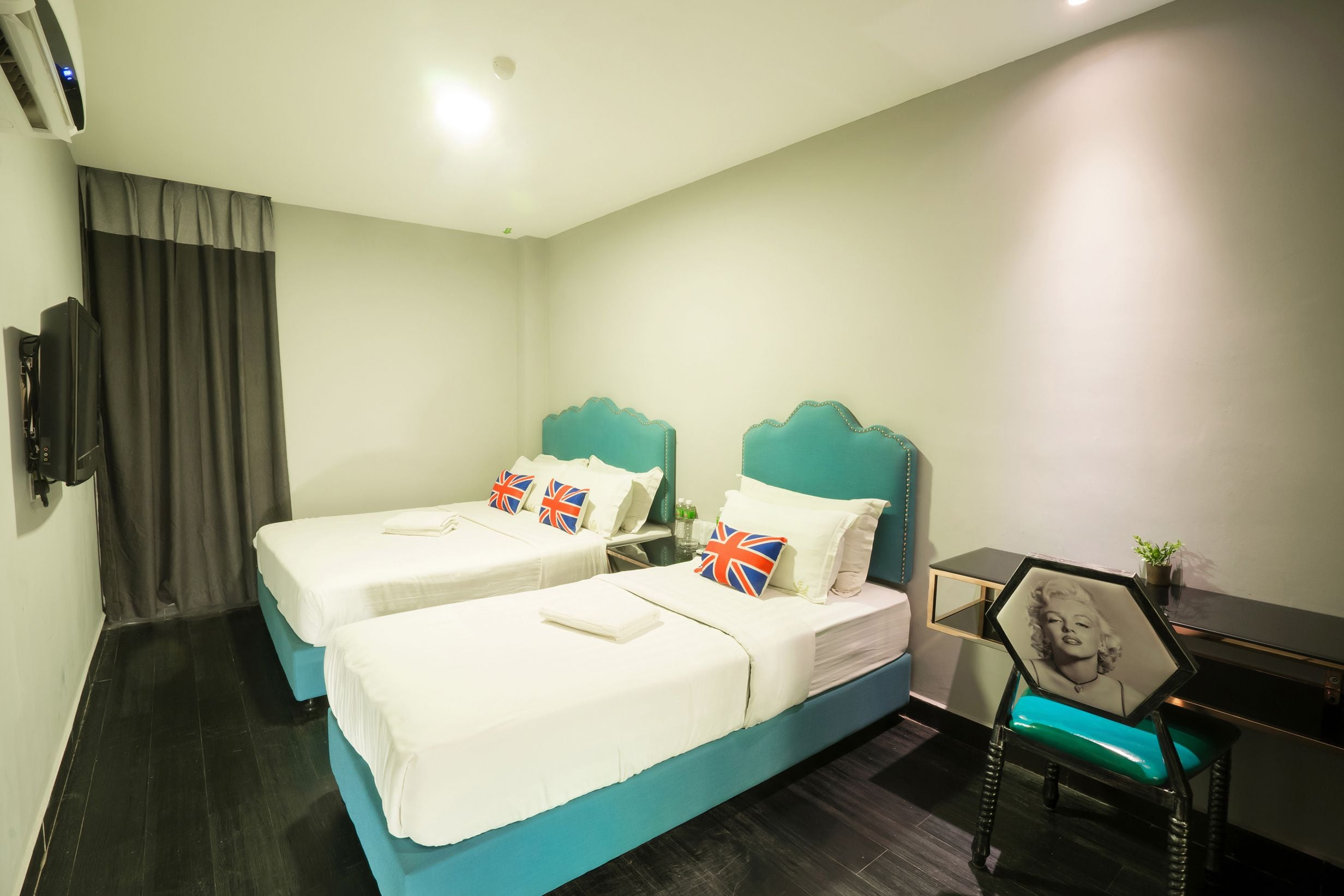 A hotel room with two beds, a desk, a chair, and a TV.