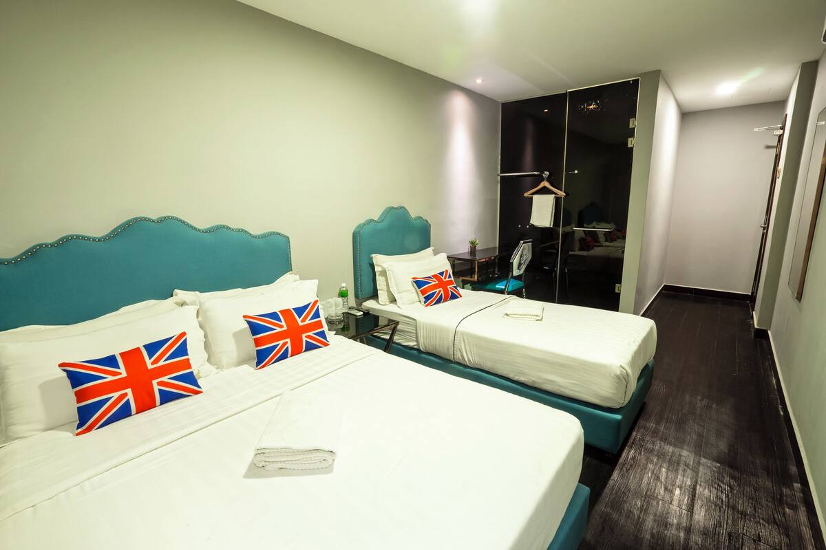 Ein Hotelzimmer mit zwei Betten, jeweils mit einem türkisblauen Kopfteil und weißer Bettwäsche. Es gibt einen kleinen Tisch mit einem Stuhl und einen Spiegel.