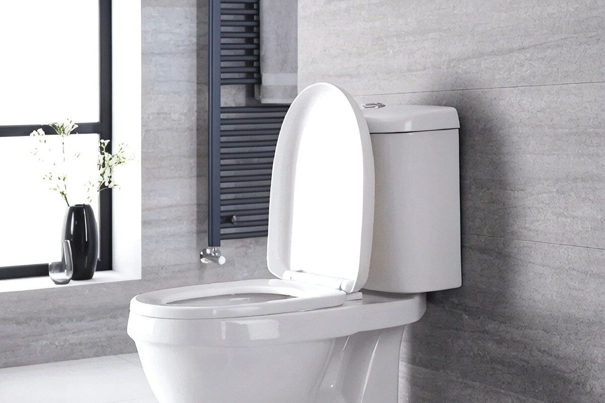 Des toilettes modernes, dotées d’un abattant fermé, installées dans une salle de bain carrelée et disposant d’une fenêtre donnant sur l’extérieur.