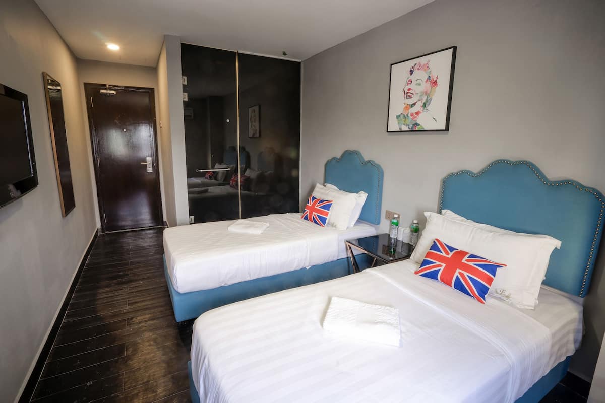 Ein Hotelzimmer mit zwei Betten, jeweils mit blauer Kopfteil und weißer Bettwäsche. An der Wand befindet sich ein Spiegel, ein gerahmtes Bild und eine Tür zu einem anderen Raum.