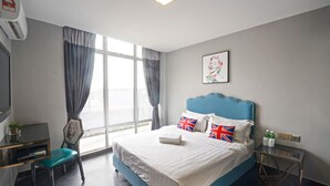 Hotelkamer met een bed, een bureau en een stoel. Er is een raam met gordijnen, een schilderij aan de muur en een tafeltje met flessen.