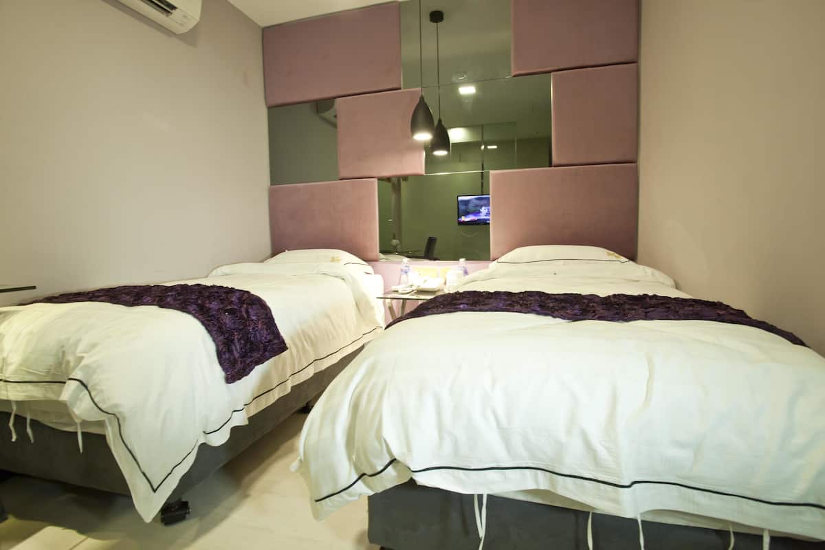 Una habitación de hotel con dos camas, un televisor y un espejo en la pared.