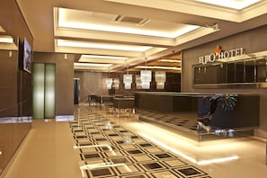 Un lobby moderno de hotel con un piso de diseño geométrico, una recepción y una gran araña.